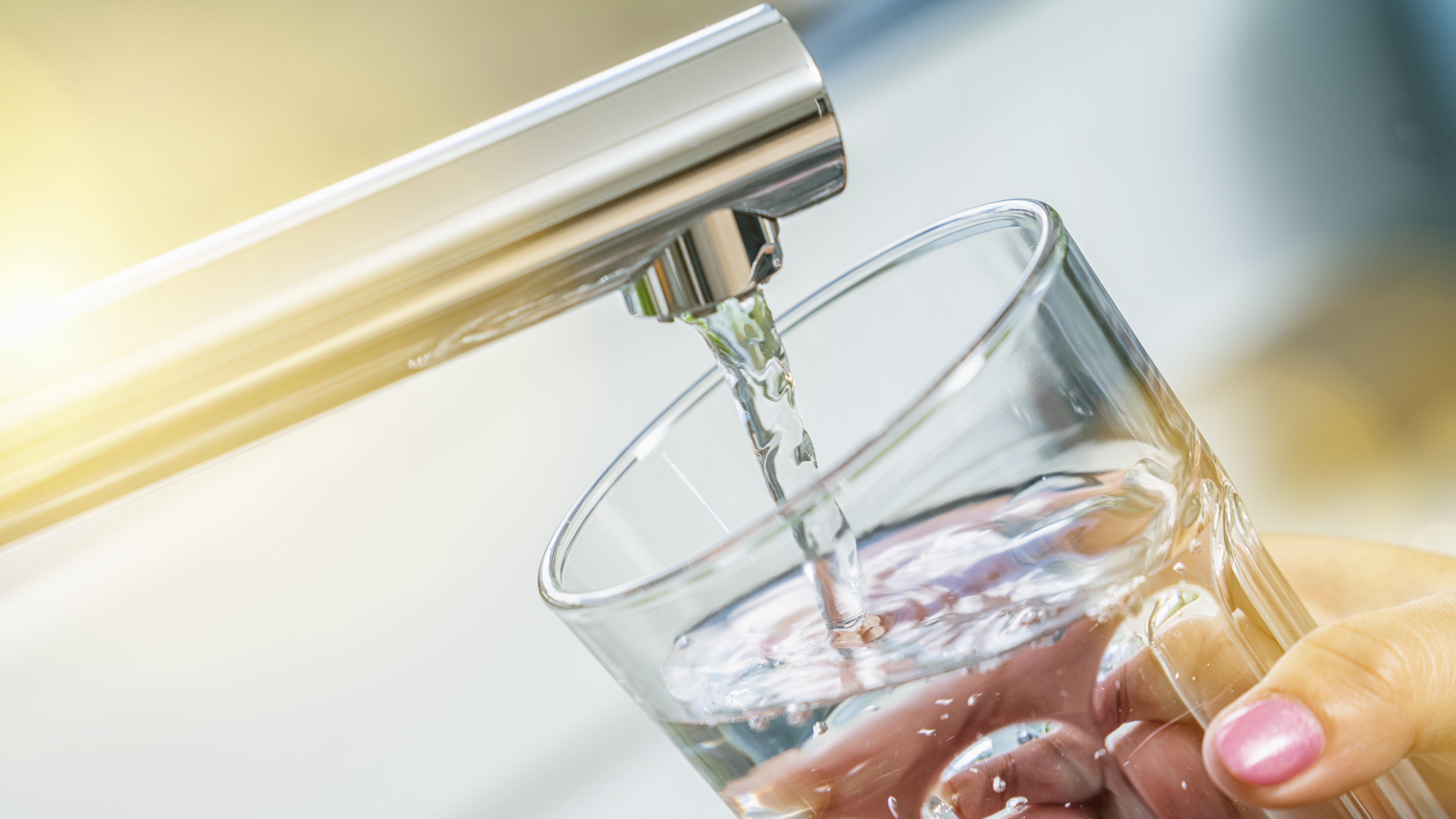 Aus dem Wasserhahn läuft sauberes Trinkwasser in ein Glas. 